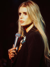 Jessica Simpson holding a microphone against a dark background