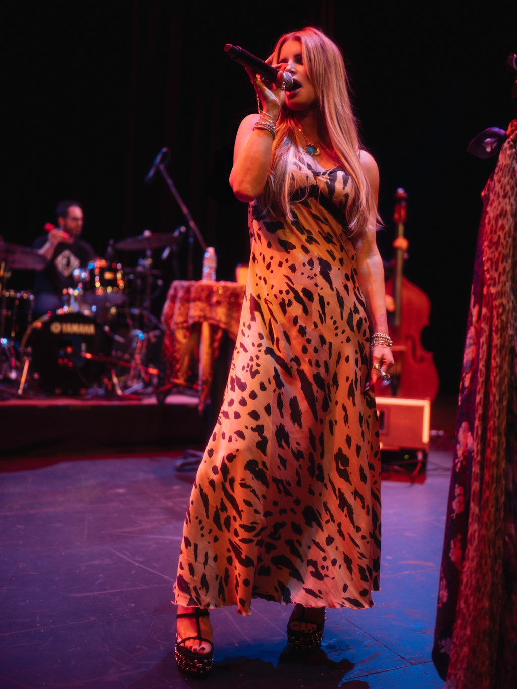 Jessica Simpson in a leopard print dress singing on stage with musical instruments in the background