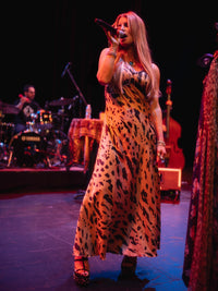 Jessica Simpson in a leopard print dress singing on stage with musical instruments in the background