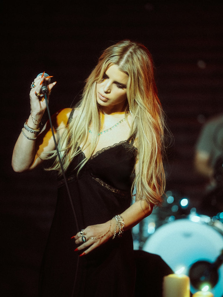 Jessica Simpson singing into a microphone on stage with a dark background