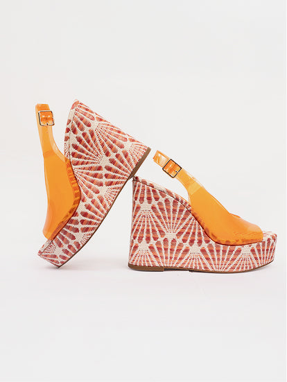 Pair of wedge sandals with orange soles and white patterned uppers on a light gray background