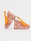 Pair of wedge sandals with orange soles and white patterned uppers on a light gray background